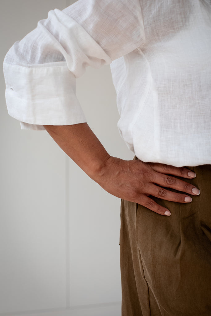 cut image of a women leaning on a sofa, wearing a white linen shirt