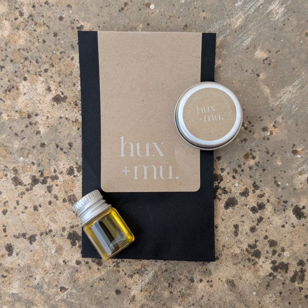 Two small samples of hux and mu earthborne skincare in a black branded envelope on a textured stone surface