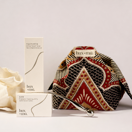 A luxury skincare set from hux+mu featuring a cotton block printed artisan pouch, full sized skincare products, face tool and rganic muslin cloth arranged on a light gray backgrounded 
