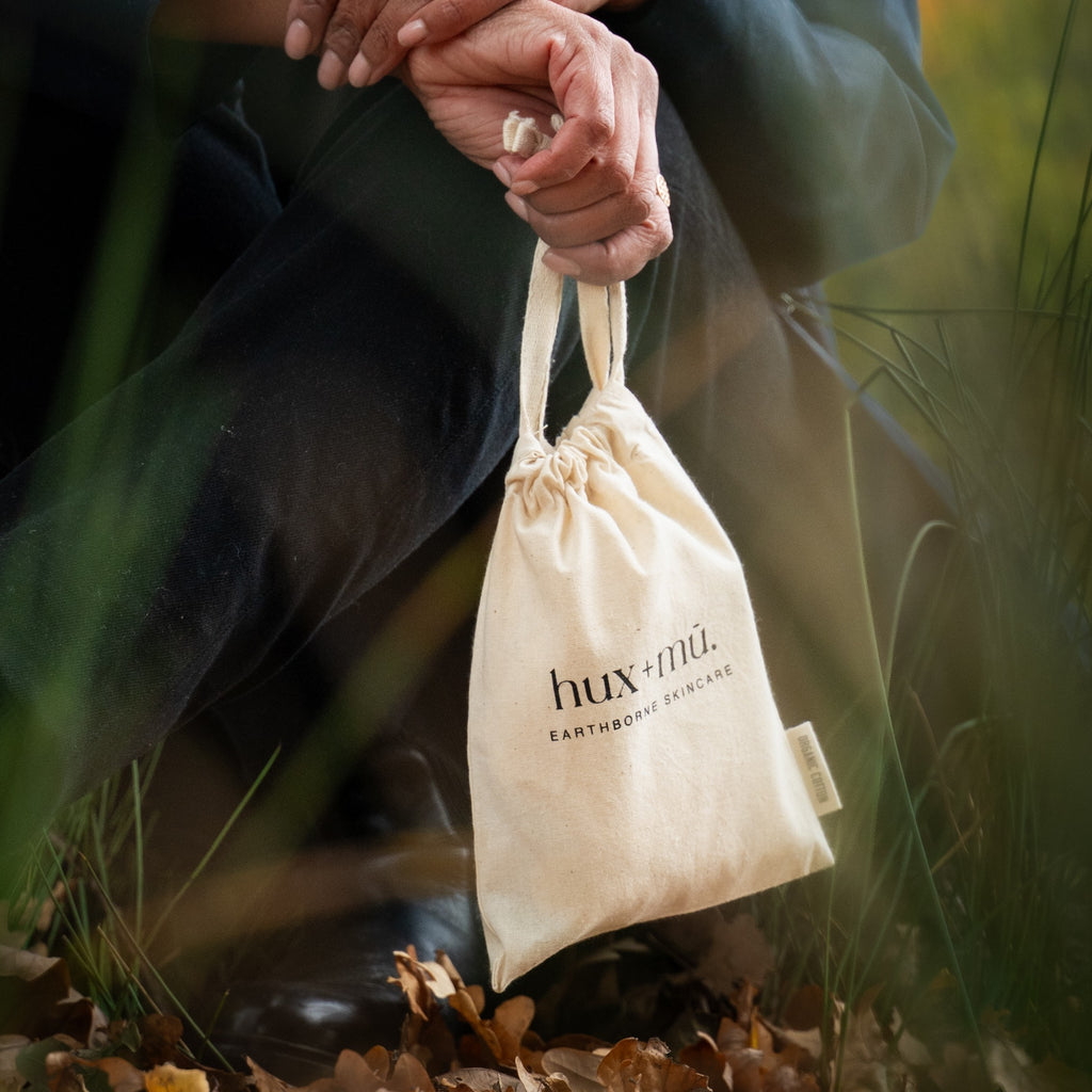 Person holding a beige drawstring bag containing the hux and mu mini mu signature ritual. In a natural setting.