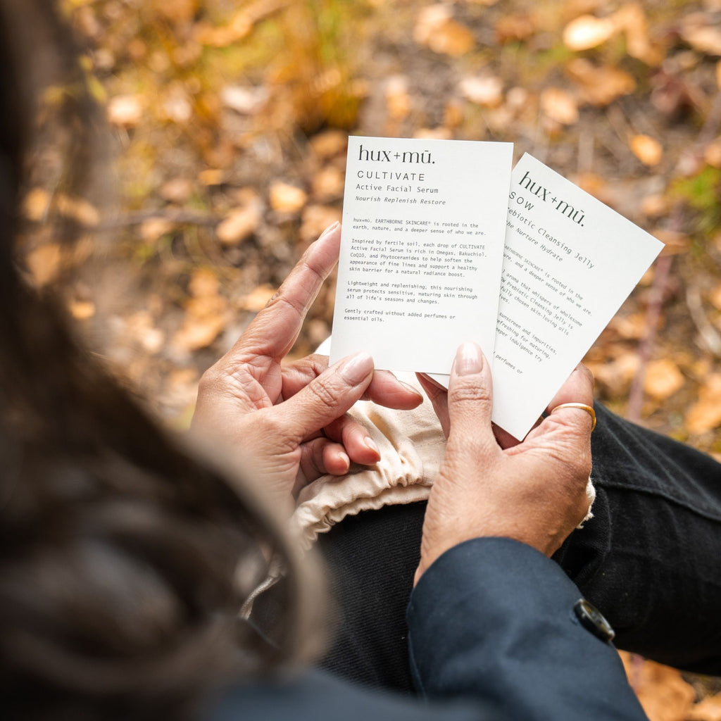 Two hands holding a 'hux and mu' product  cards with a blurred autumn background