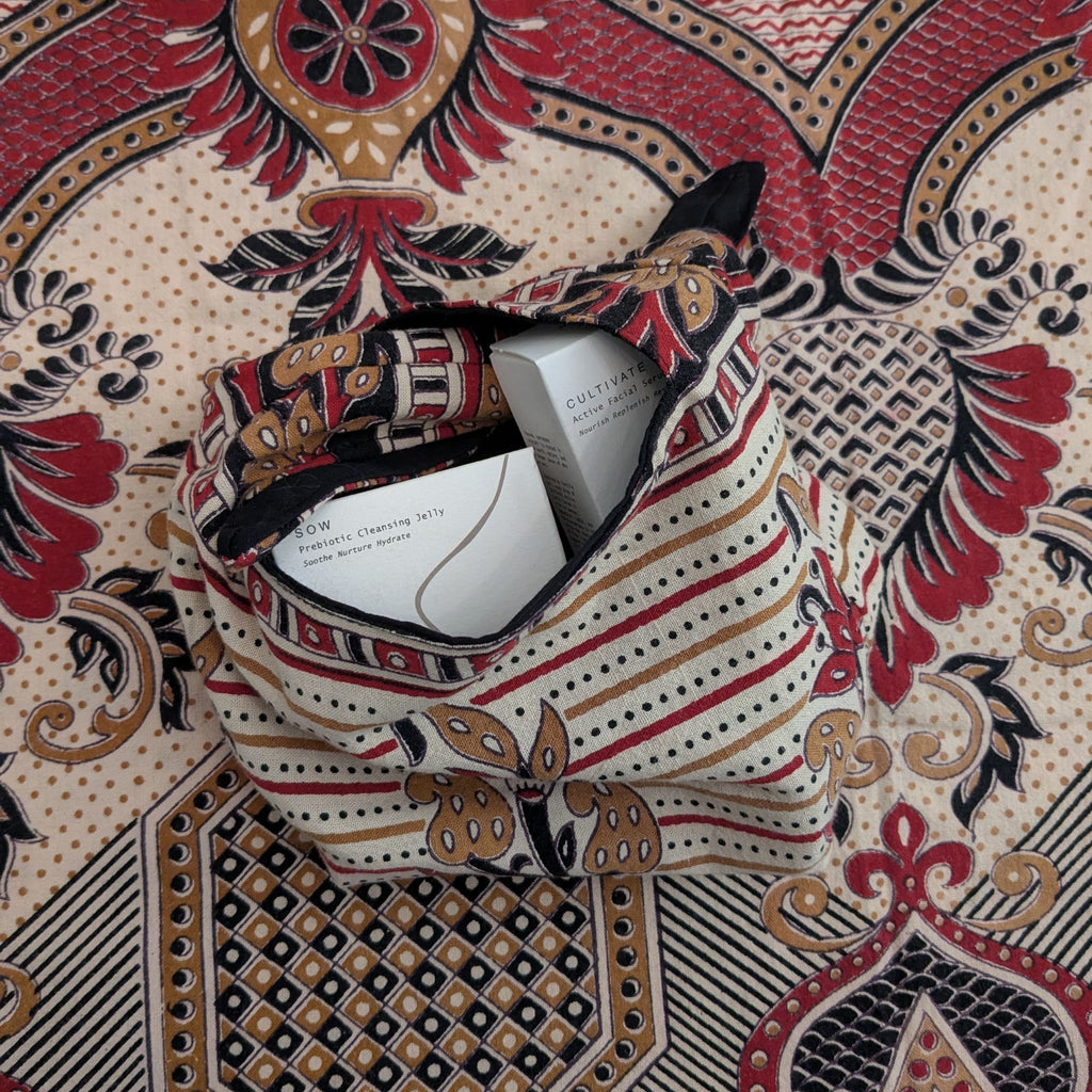Close-up of Indian hand block-printed fabric with a bag in similar fabric sitting in the centre, containing hux and mu skincare. 